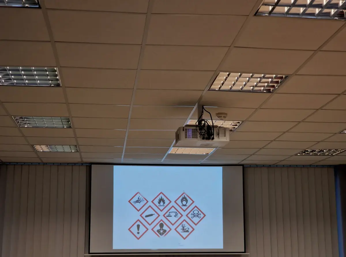 Ceiling-mounted projector displaying a slide on a pull-down screen in a training room