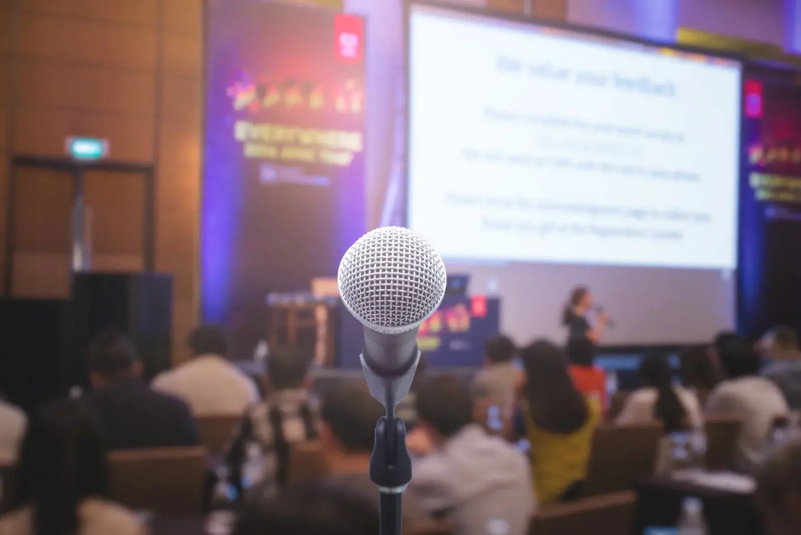 Microphone in the foreground while an audience watches projected slides