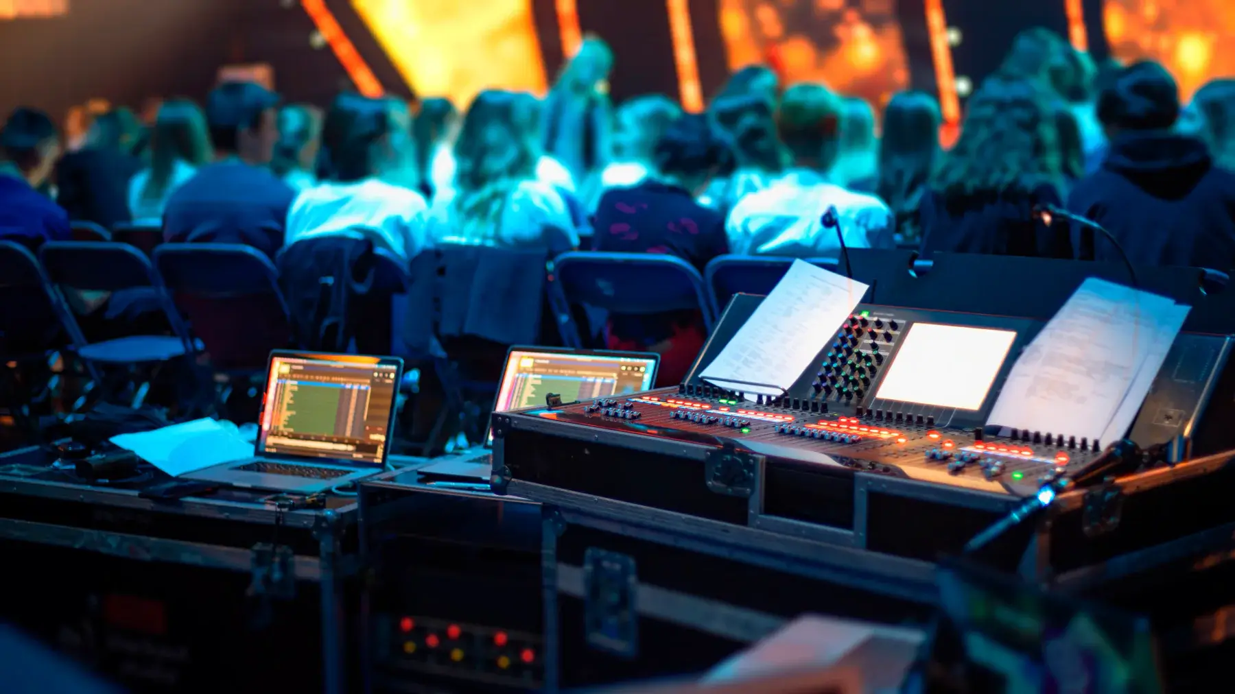 Audio console and laptops at a production desk facing an audience